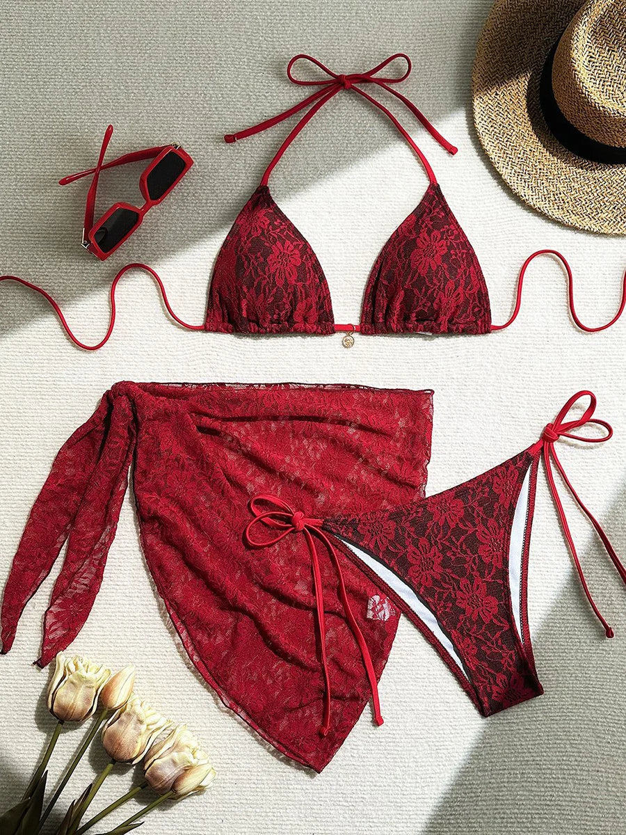 Red lace bikini set with matching cover-up, sunglasses, and hat on a neutral background.