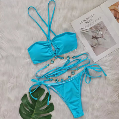 Bikinisexzy Blue bikini set with decorative straps on a textured surface with a magazine and leaf.