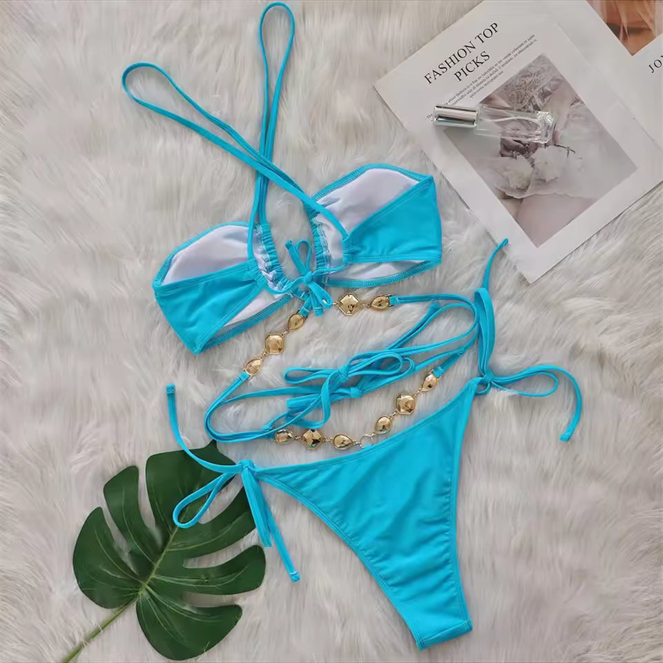 Bikinisexzy Blue bikini set with gold accents on a textured surface with a magazine and leaf.