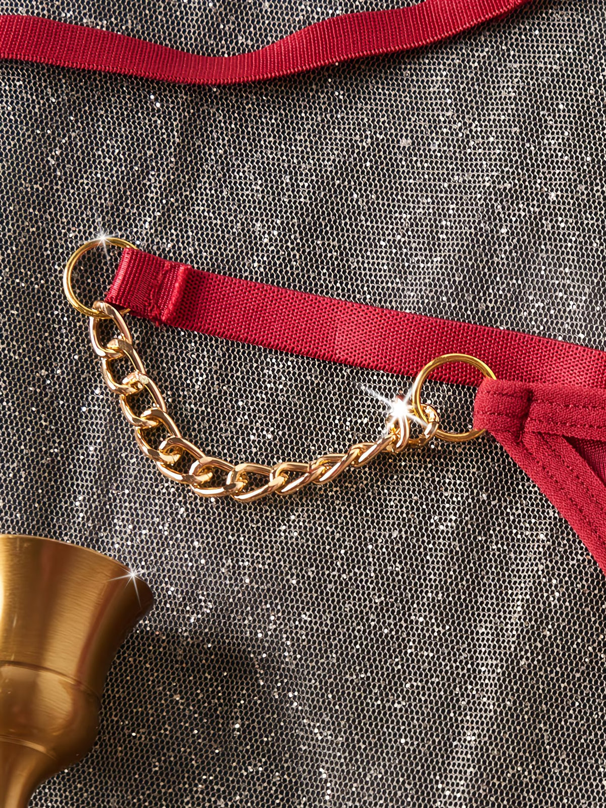 Gold chain belt with red ribbon on a textured gray surface | Detail view of gold chain straps and O-ring hardware on red lingerie set - Bikinisexzy | Bikinisexzy.com
