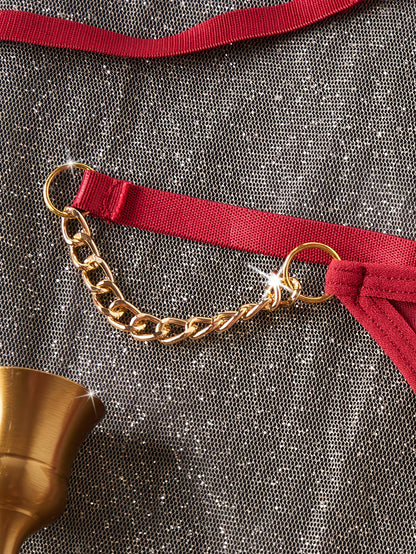Gold chain belt with red ribbon on a textured gray surface | Detail view of gold chain straps and O-ring hardware on red lingerie set - Bikinisexzy | Bikinisexzy.com