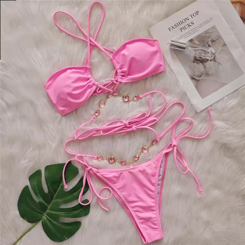 Bikinisexzy Pink bikini set with decorative strings on a textured surface with a magazine and leaf.