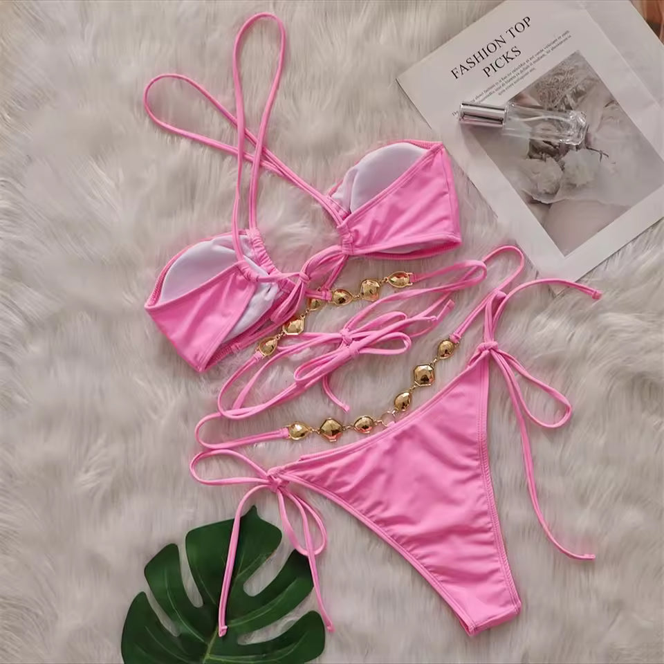 Bikinisexzy Pink bikini set with gold accents on a textured surface with a magazine in the background.