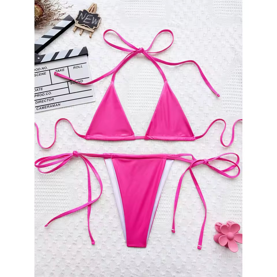Pink bikini set on a textured white surface with a clapperboard and flower decoration. BIKINISEXZY stylish faux leather bather set