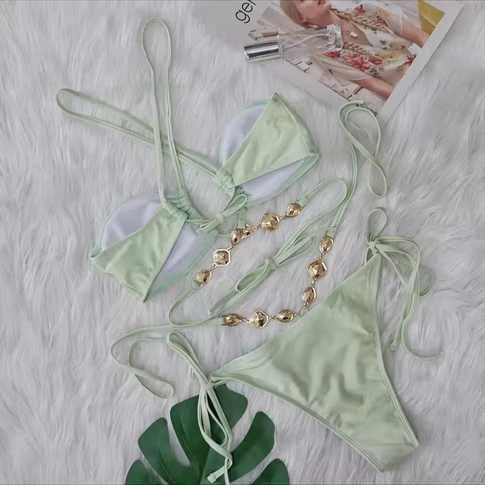 Light green bikini set with gold accessories on a textured surface.