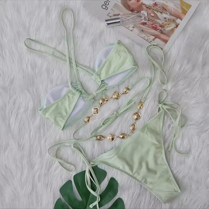 Light green bikini set with gold accessories on a textured surface.